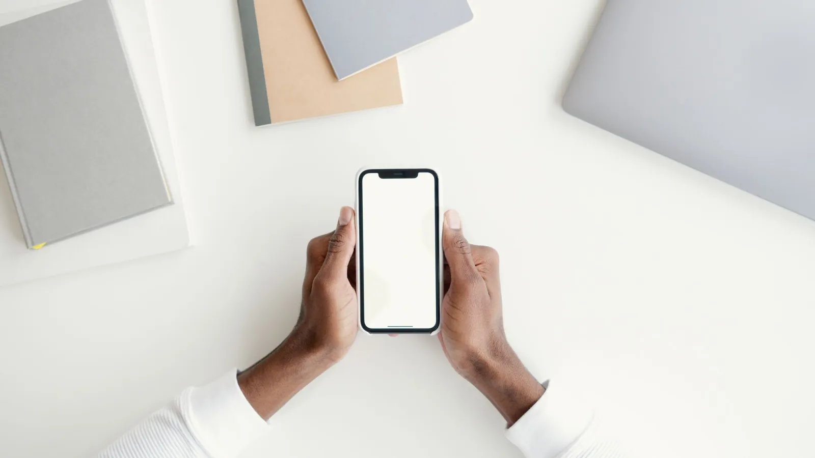 Two hands holding a phone over a white desk